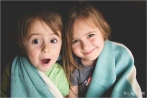 siblings smiling for the camera wrapped in green blanket