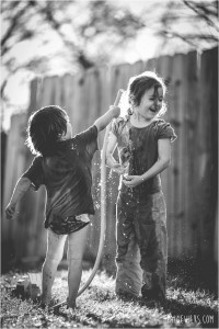 young children playing outside with water hose backlight