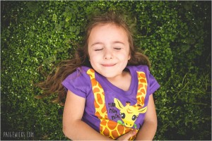 little girl smiling lying in bright green grass flowers
